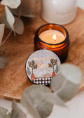 Mini Alpes candle by Mimi & August in a 2 oz size, featuring a simple white container and a lit wick for cozy ambiance.