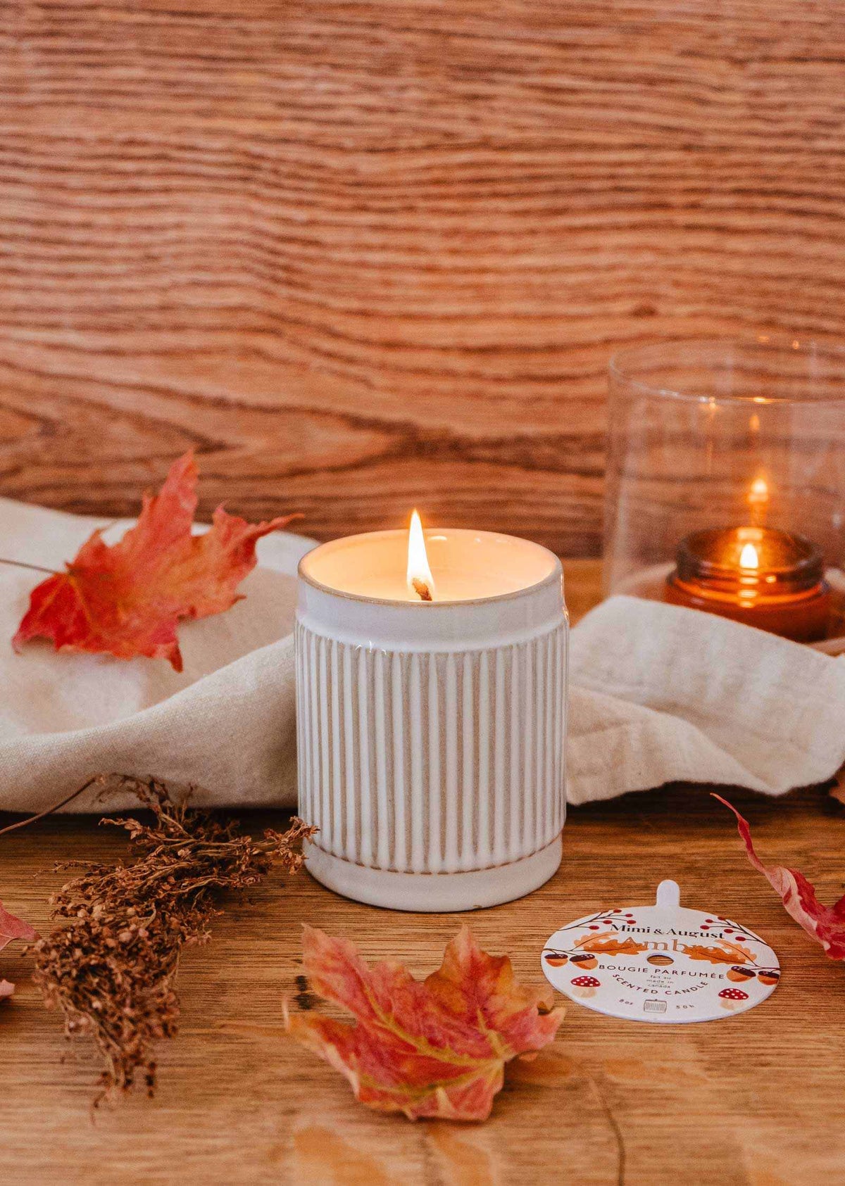 Ambre reusable soy candle by Mimi & August shown in a glass jar with a lit wick, perfect for home decor.