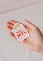 Decorative vinyl sticker of a bagel with "MTL" text from Mimi & August, ideal for customizing laptops or notebooks.