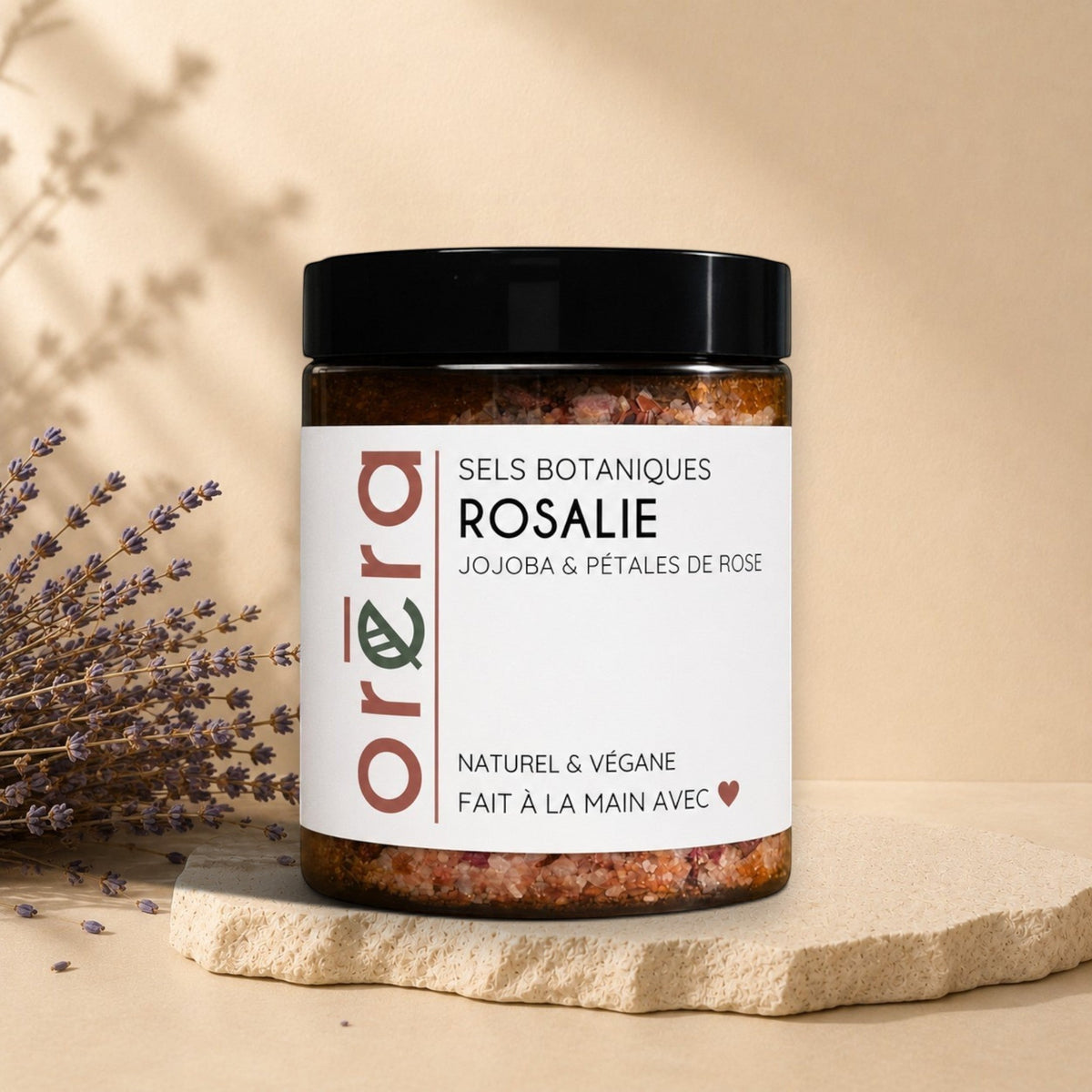 Natural bath salts with jojoba oil and rose petals from La Sultana Savonnerie, shown in a clear container with pink and white salts.