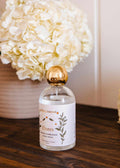 Mimi & August Flores brown ambiance room spray bottle with floral design, ideal for freshening indoor spaces.