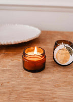 Mimi & August Woody Citrus 2 oz soy candle in a glass jar with a natural wood lid, perfect for home decor and cozy ambiance.